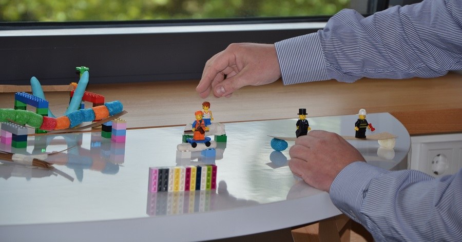 Auf einem Tisch stehen Lego-Bausteine und -figuren, die zusammen gebaut werden.