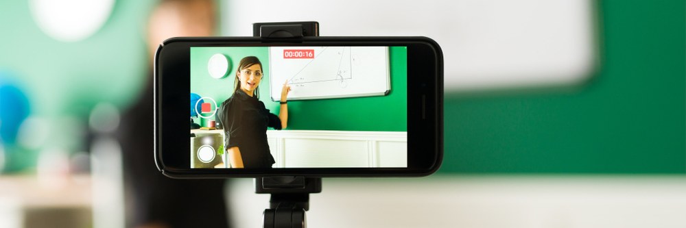 Schmuckbild einer Lehrerin vor einer Tafel, die sich mit ihrem Handy selbst filmt. Quelle: tonodiaz auf Freepik