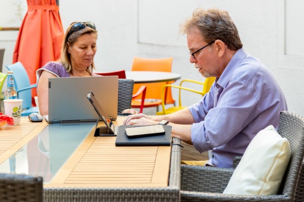 Zwei Personen sitzen am Tisch und arbeiten an ihren Laptops.