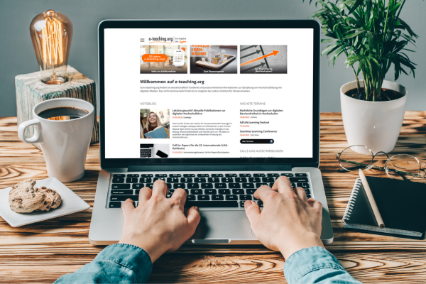 Neues Design und technisches Upgrade der Website von e-teaching.org Ein Laptop steht offen auf dem Tisch, die Startseite von e-teaching.org mit dem neuen Design ist auf dem Bildschirm zu sehen. Vor dem Laptop sind zwei Hände zu erkennen, die auf der Tastatur tippen.