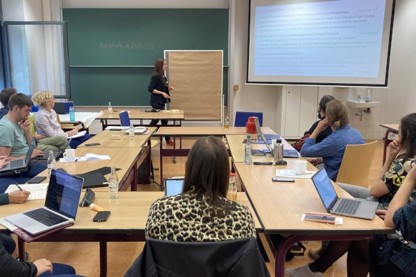 Bilanzierungstagung der AG Didaktische Metadaten (Hochschule) Mehrere Personen sitzen in einem Seminarraum. Vorne wird eine Präsentation gezeigt.