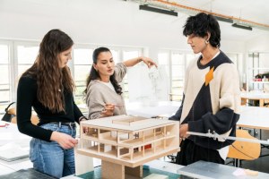 Projektlernen Drei junge Menschen stehen um ein 3D-Haus- bzw. Architekturmodell und diskutieren miteinander.