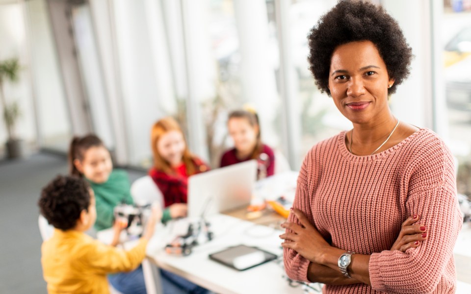 Lehrerin steht vor Schülerinnen und Schülern während einer Gruppenarbeitsphase mit Robotern